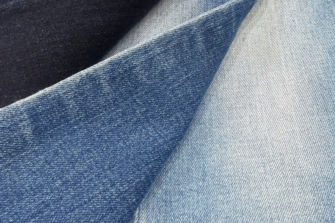 Cận cảnh mặt vải denim xanh chàm gấp nếp, thấy rõ đường gân chéo, vệt bạc và đường chỉ cam