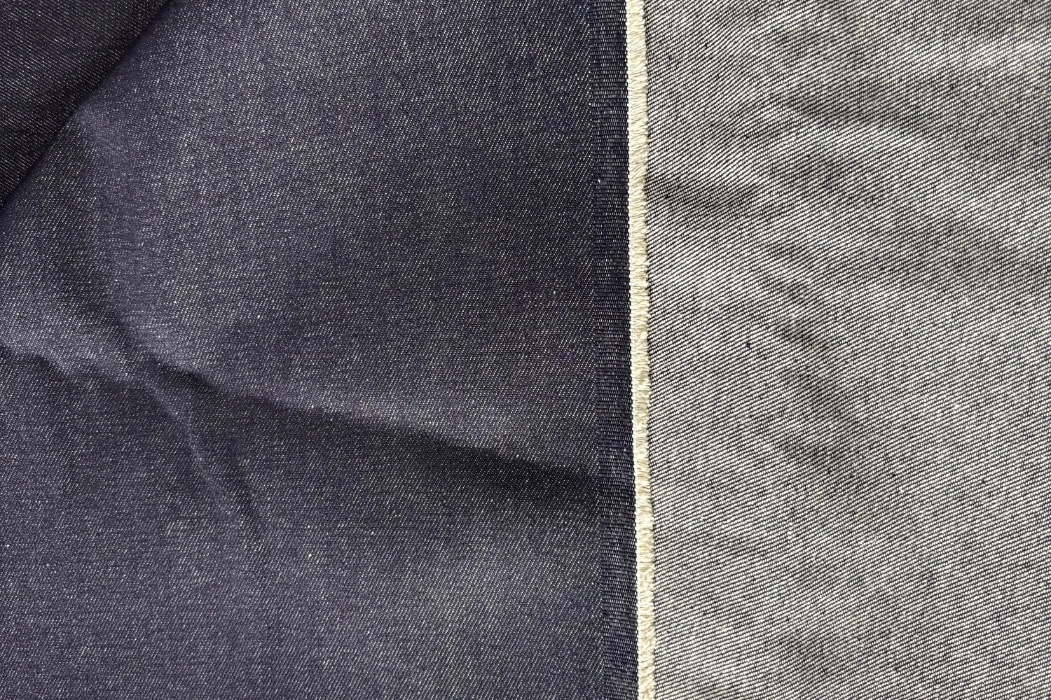 Tấm vải denim xanh chàm gập chéo, bên phải là dải biên vải dệt chặt màu xám nhạt chạy dọc, khác hẳn phần thân vải