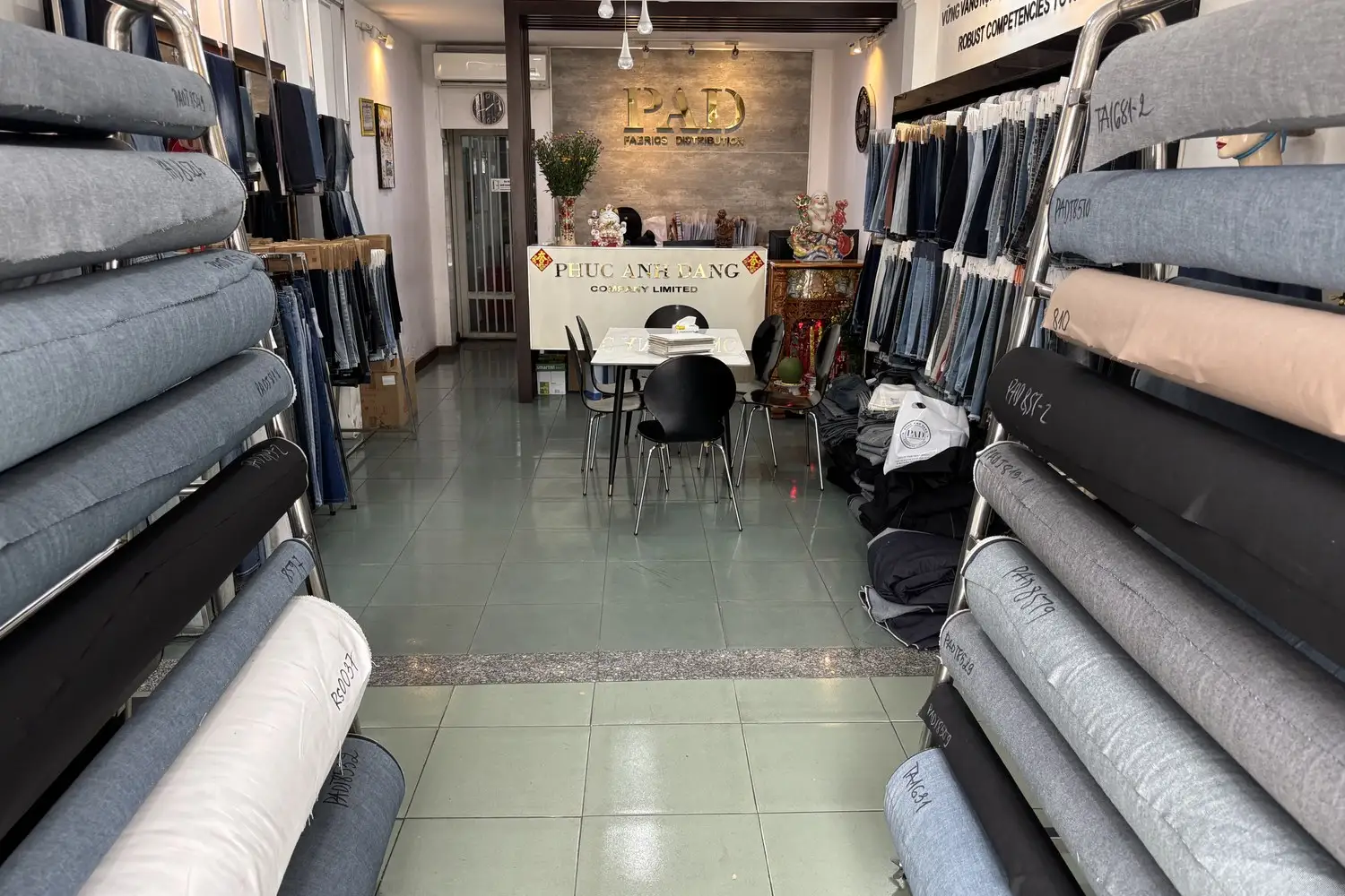 Kho vải của Phúc Anh Đăng, các cây vải jean xám và xanh cuốn chặt xếp trên kệ inox và nằm dưới sàn, nhìn về phía quầy lễ tân