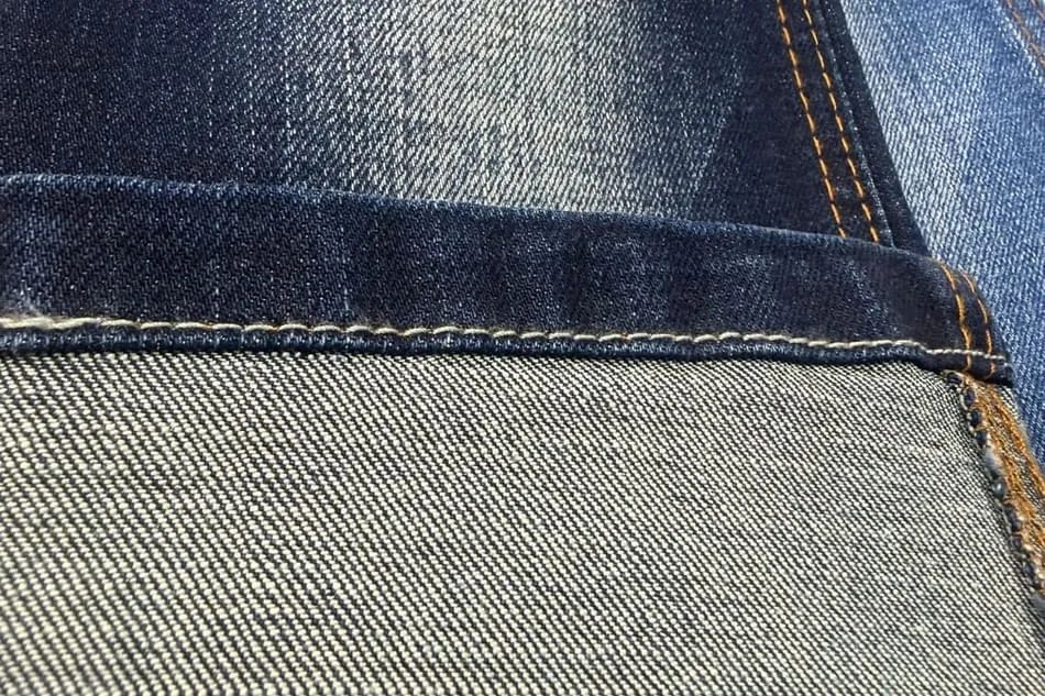 Ống quần denim gấp ngược, mặt ngoài xanh chàm đậm nằm trên, mặt trong lộ ra gần như trắng bạc