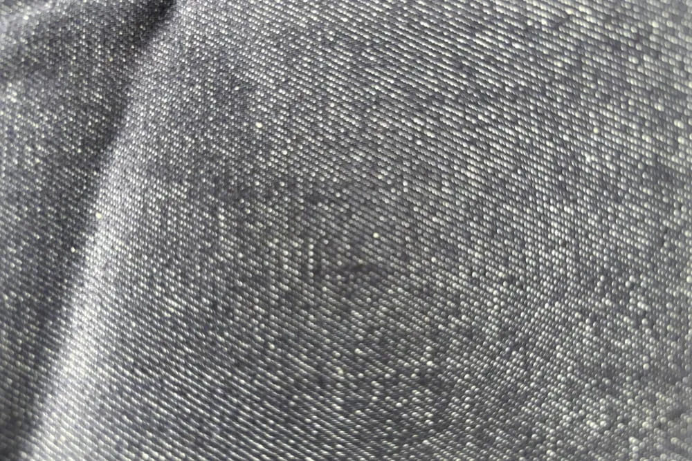 Cận cảnh mặt vải denim xám, thấy rõ những đường gân chéo song song chạy nghiêng khắp bề mặt