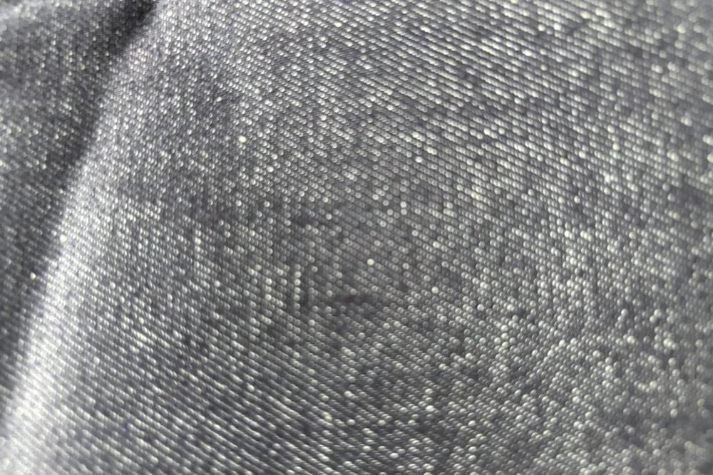 Cận cảnh mặt vải denim, thấy rõ từng sợi dọc sẫm màu và sợi ngang trắng đan chéo nhau