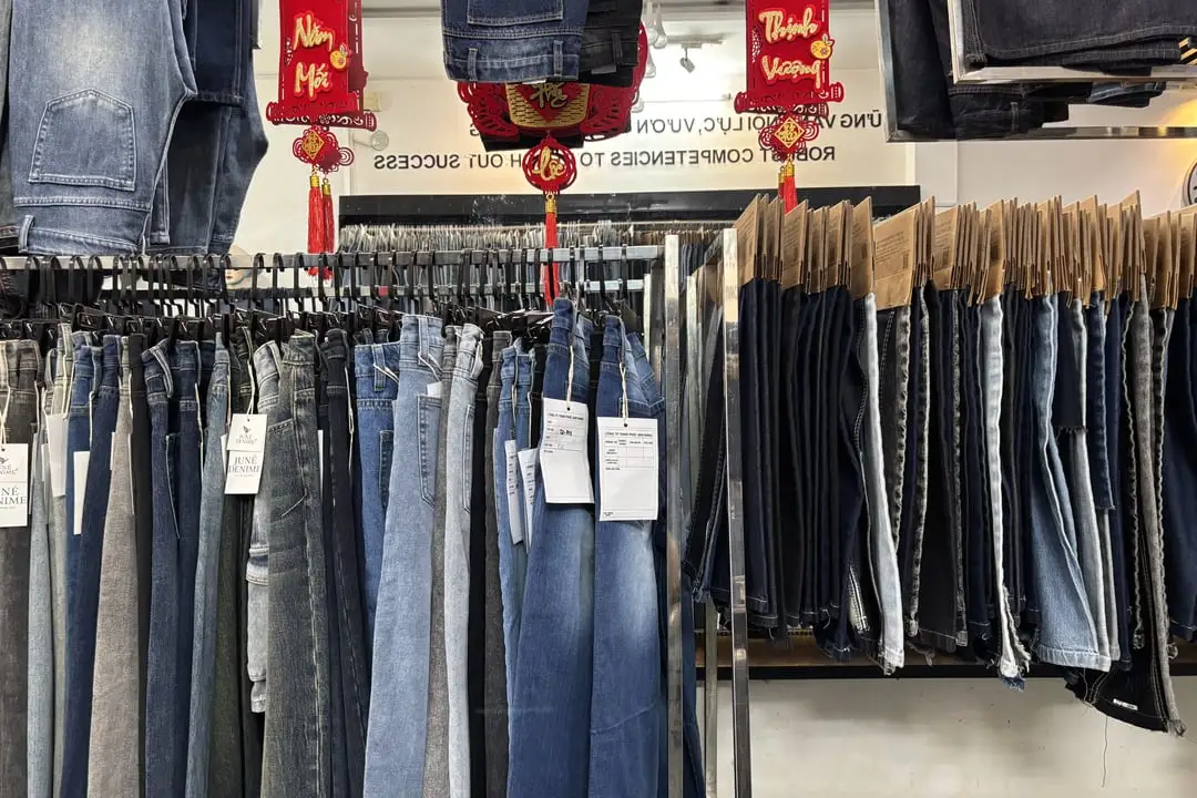 Giàn quần jeans nhiều màu wash treo trên móc, bên phải là hàng dài mẫu vải jean kẹp tag giấy trong cửa hàng Phúc Anh Đăng