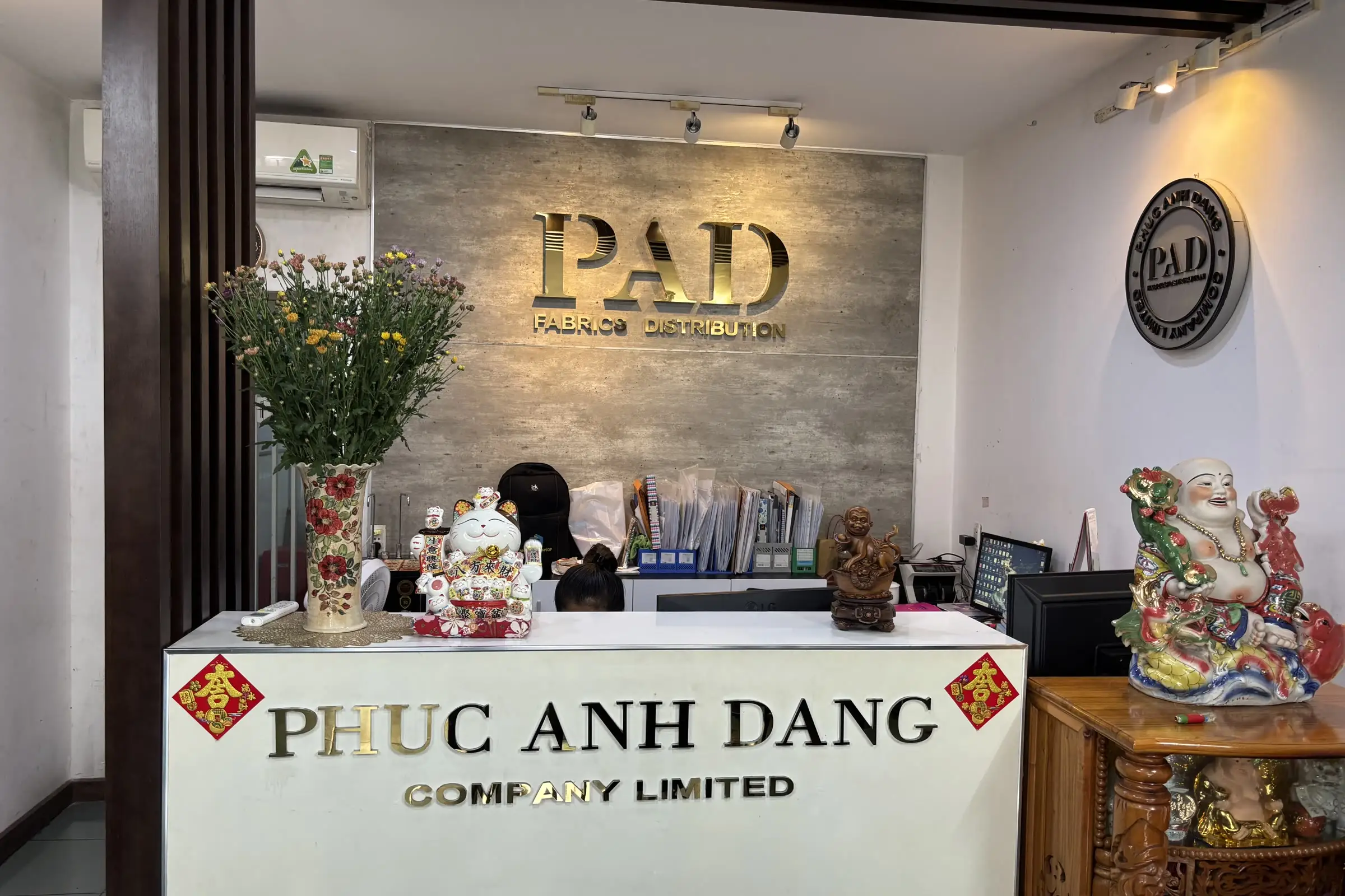 Quầy tiếp khách của Công ty TNHH Phuc Anh Dang, phía sau là bức tường ốp gỗ gắn chữ PAD Fabrics Distribution
